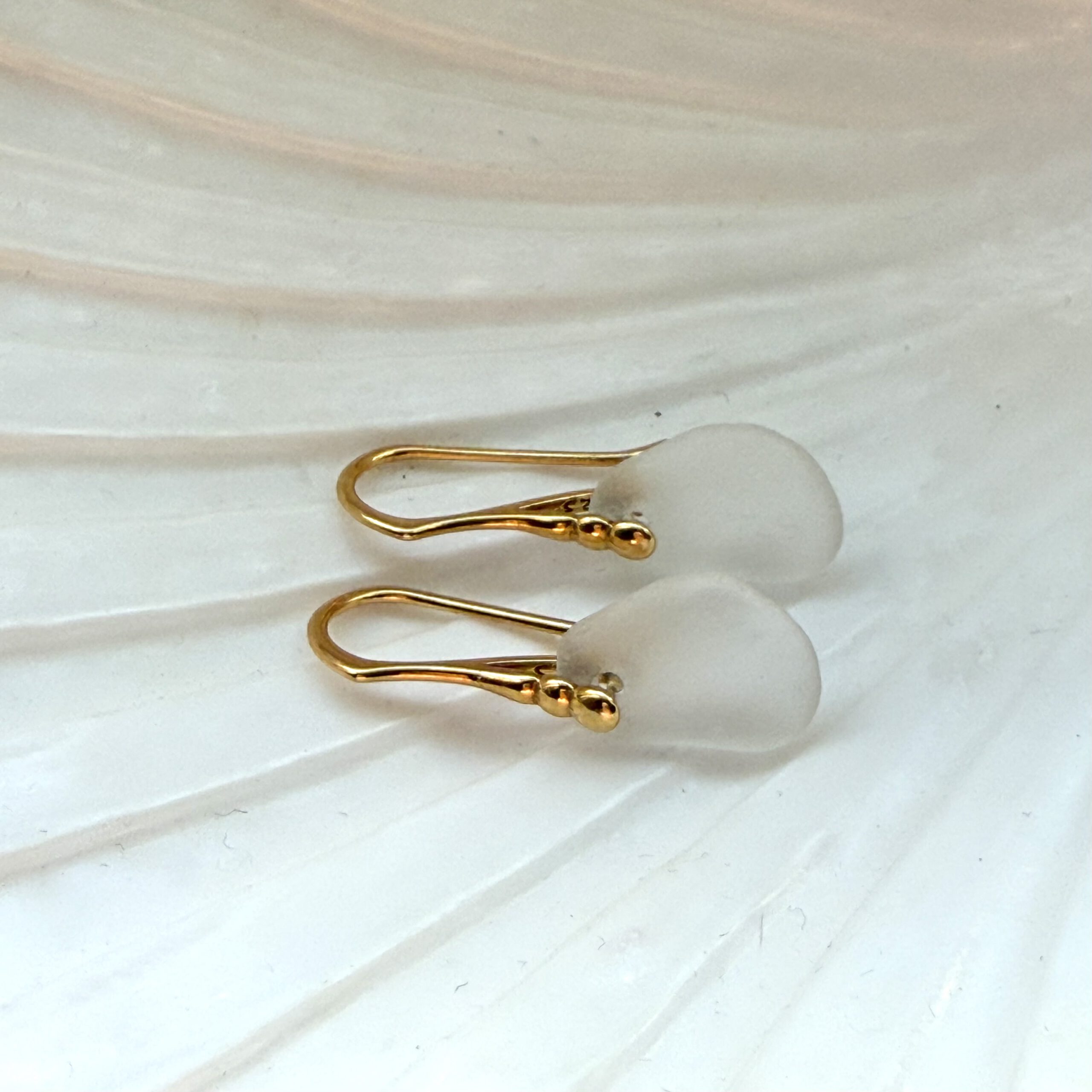 witte zeeglas oorbellen met gouden oorhaakjes liggend