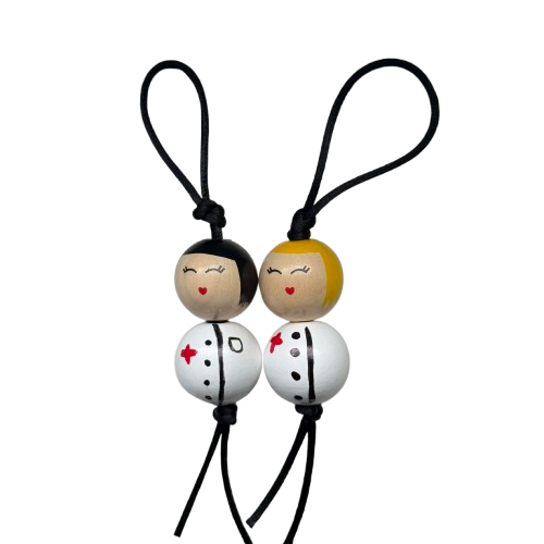 Twee houten zuster gelukspoppetjes naast elkaar, met geel en zwart hoofdje, elk handbeschilderd in wit zusteruniform.