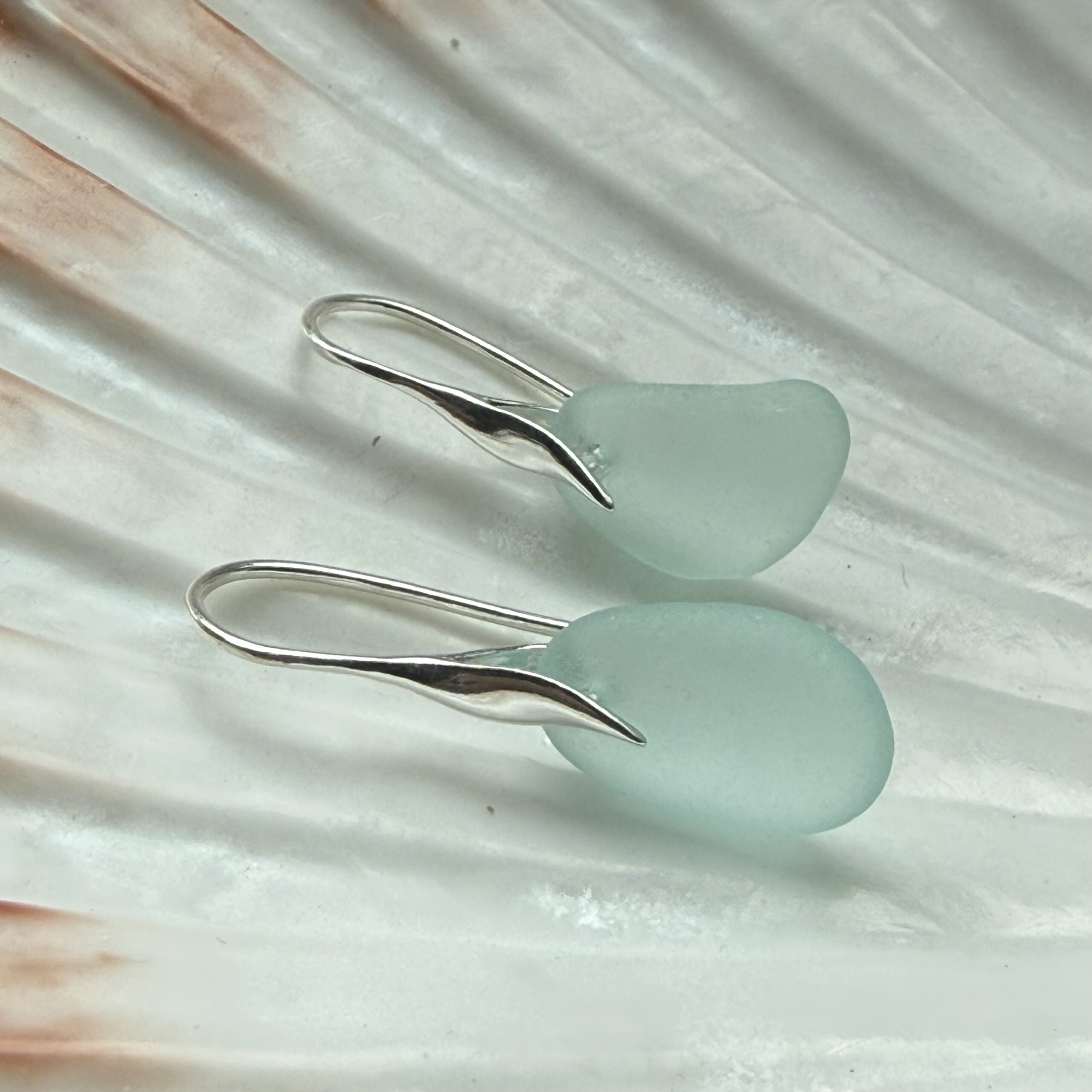 aqua zeeglas oorbellen met zilveren haakjes liggend op een schelp