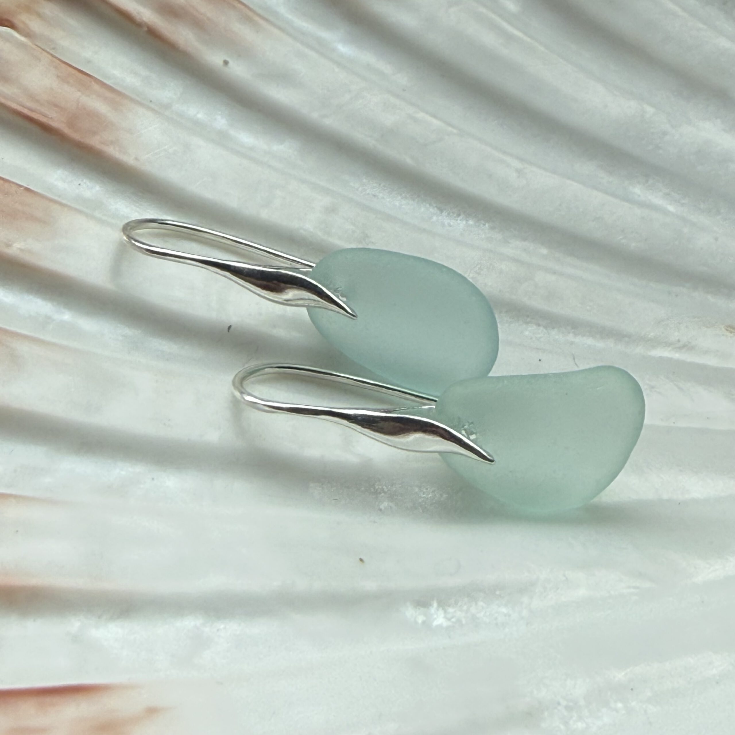 auqa zeeglas oorbellen met zilveren haakjes liggend op een schelp