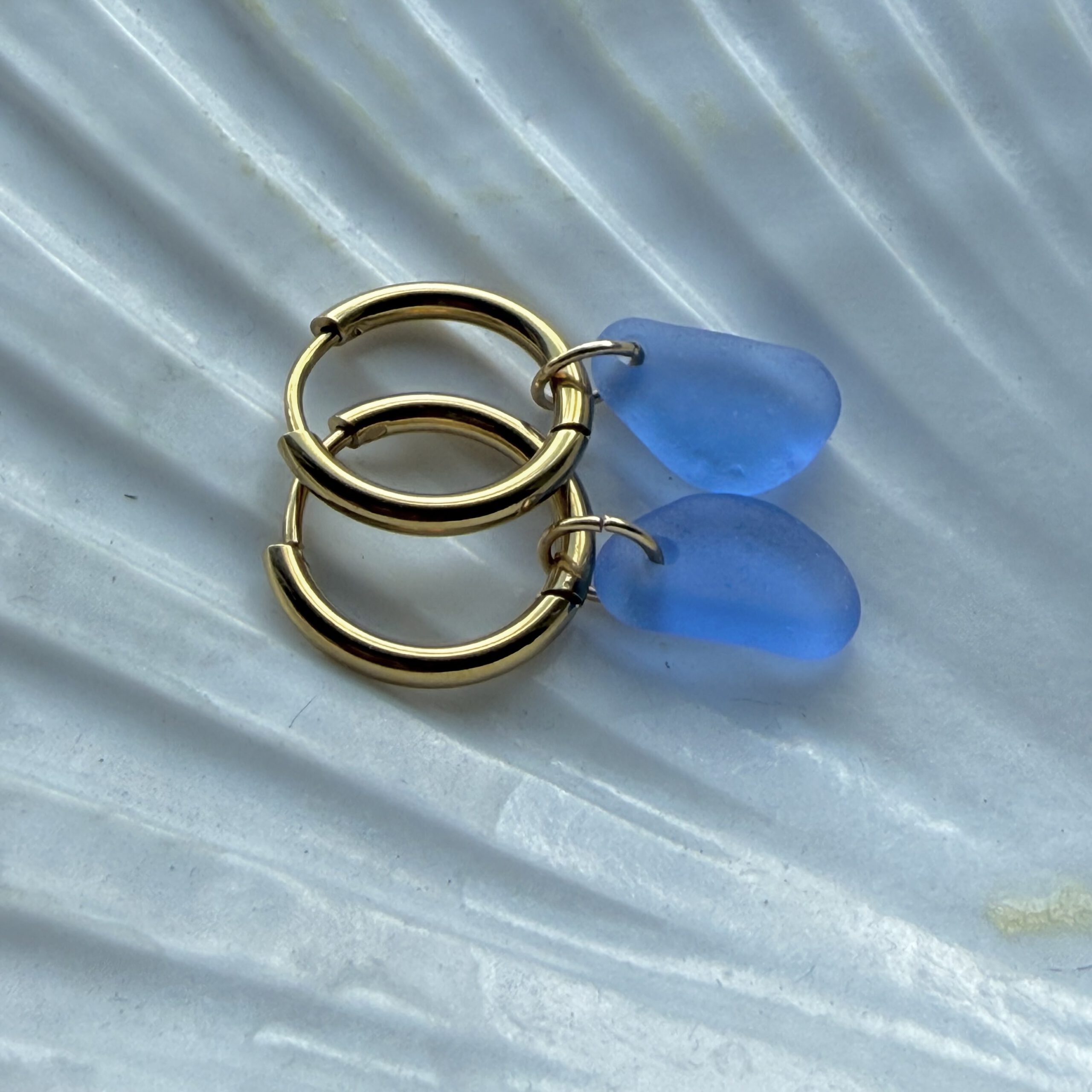 blauwe zeeglas oorbellen liggend op schelp