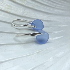 blauwe zeeglas oorbellen met zilveren haakjes liggend op een schelp