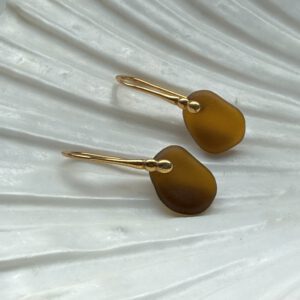 Bruine zeeglas oorbellen met een zilveren oorhaakjes liggend op een schelp
