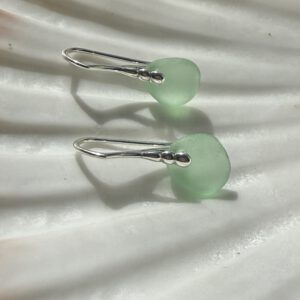 zeeglas lichtgroen zilver oorbellen liggend op een schelp