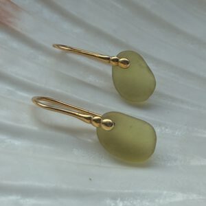 zeeglas olijfgroen oorbellen liggend op een schelp