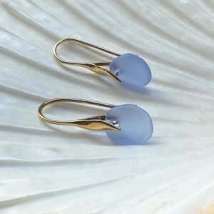 paarse zeeglas oorbellen met gouden haakjes liggend op een schelp
