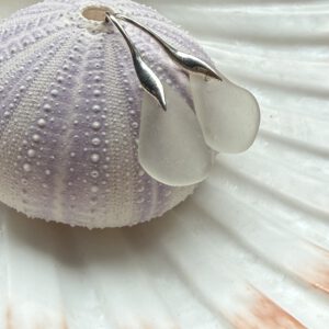 witte zeeglas oorbellen met zilveren oorhaakjes hangend aan zeeegelschelp