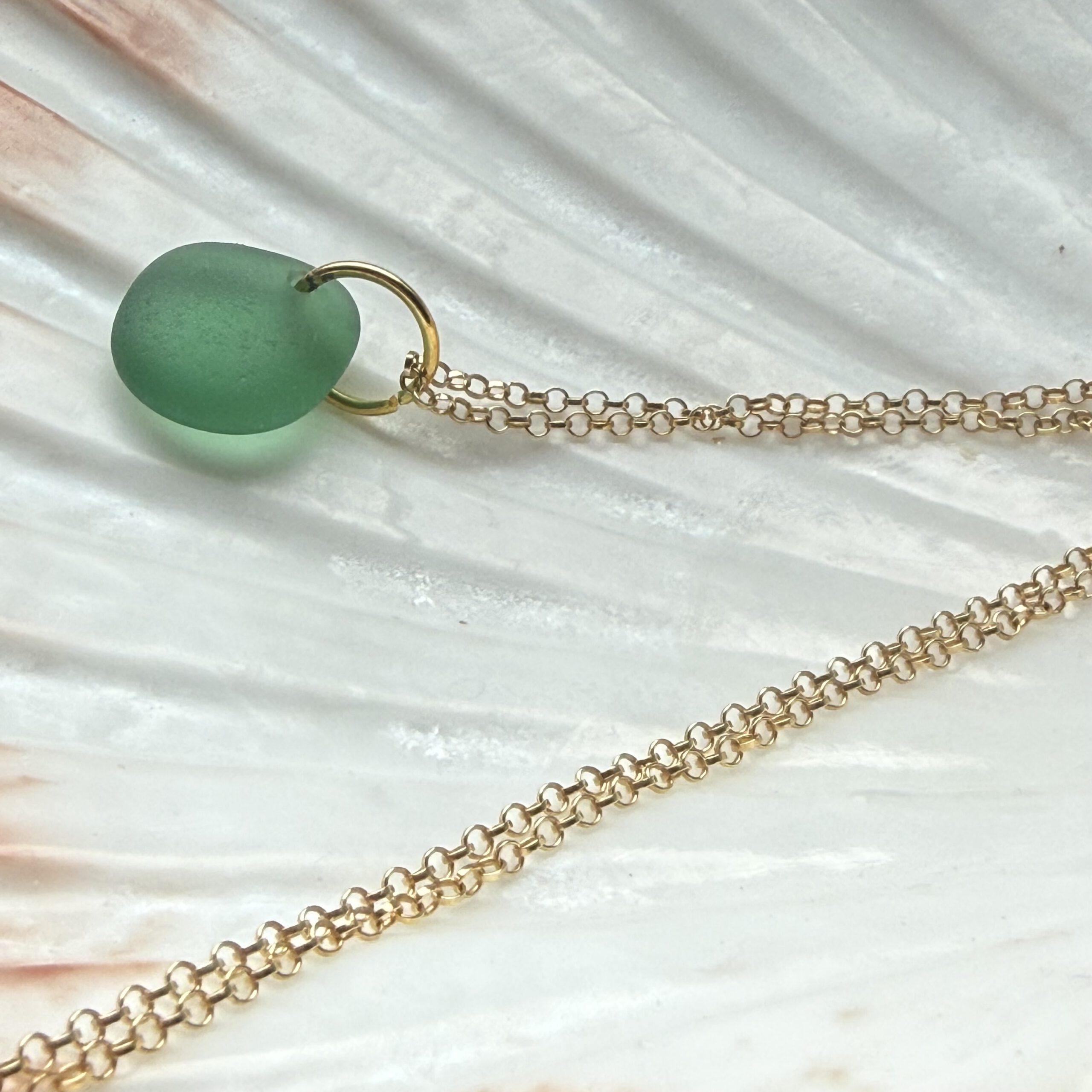 zeeglas bosgroen goud ketting liggend op een schelp