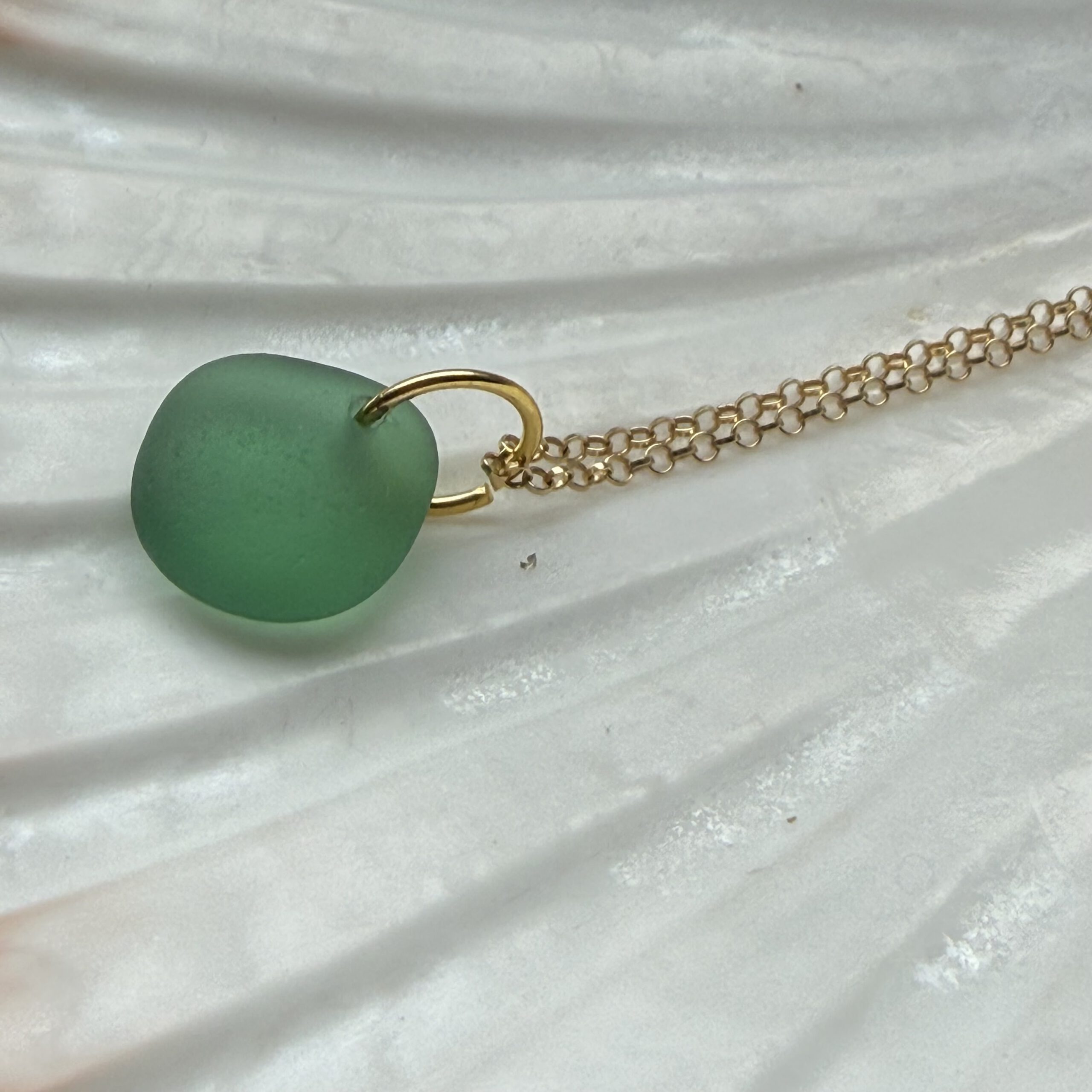 zeeglas bosgroen goud ketting liggend op een schelp