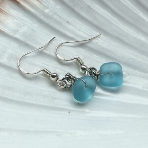 zeeglas oorbellen lichtblauw zeeglas liggend op een schelp
